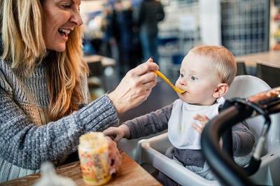 Woman foster carer smiling and feeding a baby in a high chair