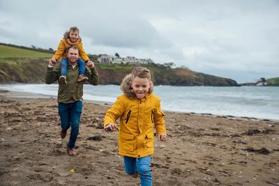 Man on beach with young boy on shoulders and young boy running in front of him