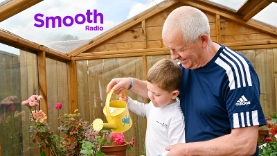 Older man watering flowers in a greenhouse with young boy Older man watering flowers in a greenhouse with young boy